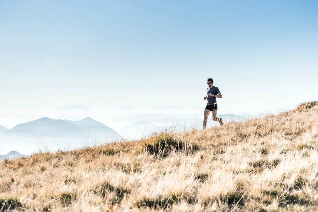 man running through a field in the mountains