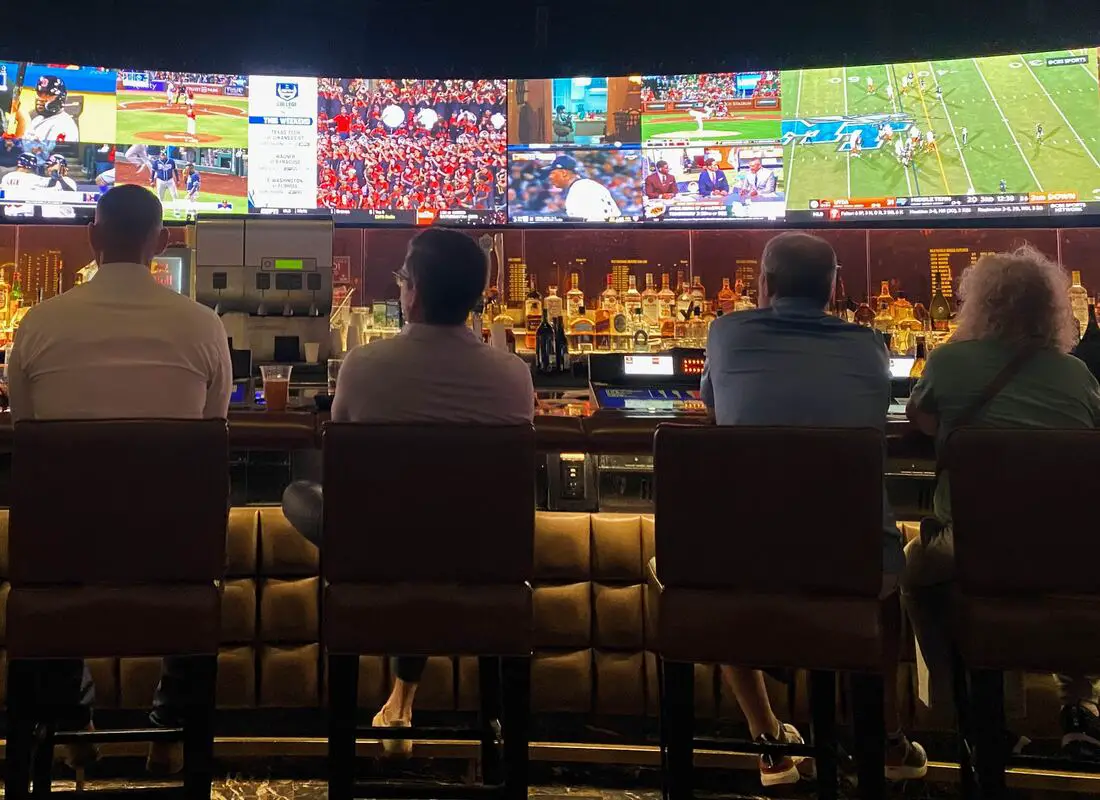 4 people sitting at a bar in a las vegas sportsbook watching games on tv